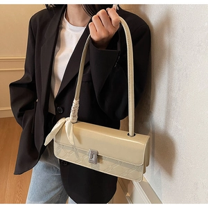 Detail of beige faux leather handbag with embossed patterns and decorative silk scarf