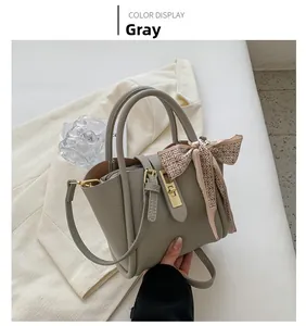 Détail du sac seau en cuir gris avec foulard en soie rose et finitions dorées
