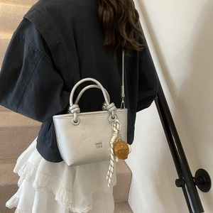 Detail of silver textured leather bucket bag with creative cookie charm on a model