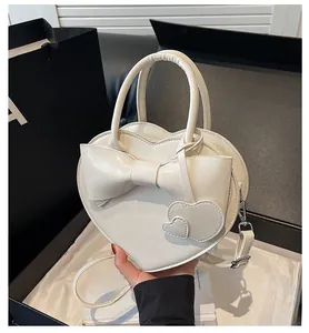 Detail of white heart-shaped handbag featuring a large bow and twin heart charms