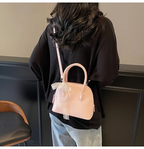 Détail du sac à main rose en cuir grainé avec charm nœud en dentelle blanche sur le côté