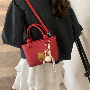Close-up of bright red bucket bag with litchi texture and baseball charm on a model