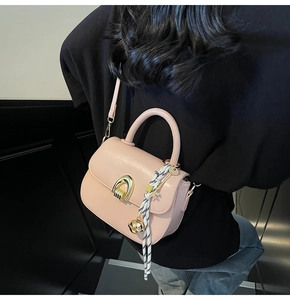 Detail of light pink mini handbag with woven tassel and gold hardware worn by a model