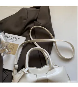 Detail of white leather shoulder bag featuring a large bow and long smooth strap