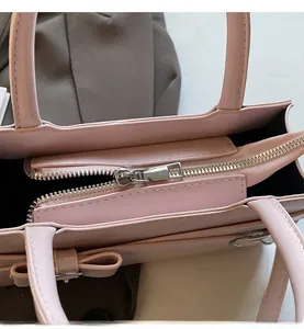 Detailed macro view of the smooth metal zipper and bow decor on this pink square handbag