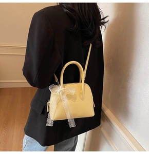 Gros plan d'un sac à main jaune en forme de coquille avec un nœud en dentelle blanche