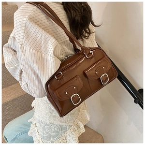 Detail of large brown patent leather pillow bag with metal buckles and twin handles
