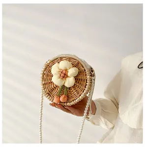Detail of round woven straw bag with floral accents and elegant pearl chain strap