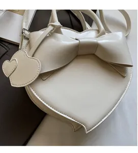 Detail of cream heart-shaped crossbody bag featuring a large bow and leather charms