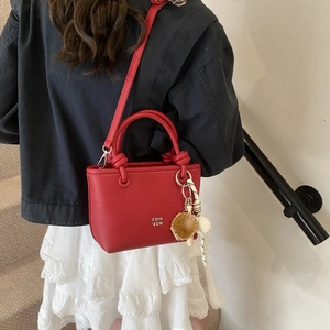 Macro shot of red leather tote bag with sporty charms and white logo on white outfit