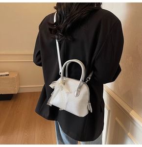 Mini sac dôme argenté en cuir grainé avec nœud en dentelle blanche sur un banc en pierre