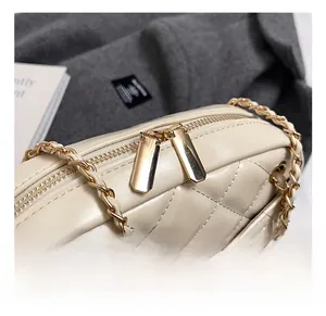 Detail of cream quilted square bag showing gold metal chain and dual zippers close-up