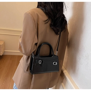 Crossbody view of black matte leather square bag with bow detail on a camel blazer