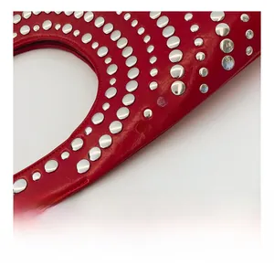 Détail de la texture du cuir rouge et des rivets en métal argenté poli du sac à main