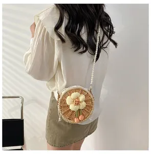 Detail of hand-woven round rattan bag with floral motif and white pearl chain strap