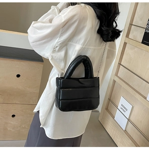 Detailed side view of black quilted bucket bag with silver chain strap worn by a model