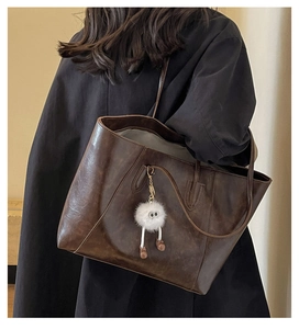 Detail of glossy brown leather tote bag with a cute white plush monster keychain