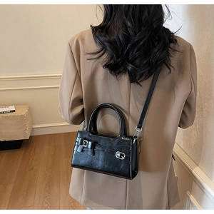 Detail of black glossy leather crossbody bag with silver buckle and thin strap on a blazer