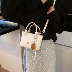 Close-up of a white minimalist bucket bag with a creative baseball glove charm detail