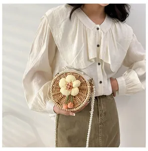 Detail of round woven rattan bag with 3D floral accent and elegant pearl chain strap