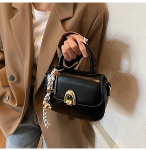 Detail of black semi-circular handbag with golden U-lock and woven decorative lanyard