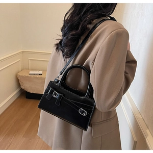Detail shot of a black patent leather crossbody bag with a decorative bow and silver buckle