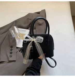 Détail du sac coquillage noir en cuir grainé avec grand nœud en dentelle blanche et anses