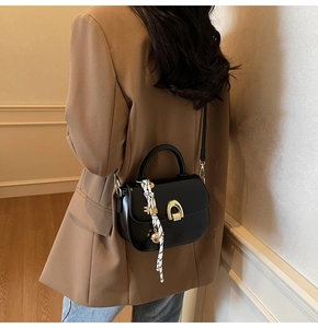 Detail of black leather handbag with golden clasp and decorative silk scarf on the handle