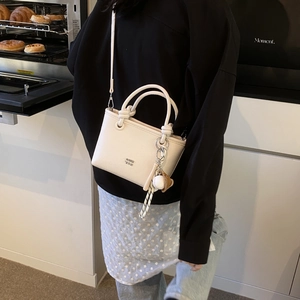 Detail of off-white leather handbag with knot handle and baseball charm on a model