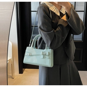 Detail of light blue crossbody bag with bow decoration and silver buckle worn on dark blazer