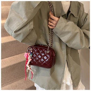 Detail of burgundy quilted chain bag featuring a heart pendant and woven strap