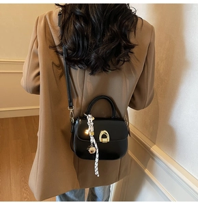 Black leather crossbody bag with gold buckle and silk scarf on a camel blazer