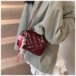 Detail of burgundy quilted chain bag with colorful floral charm worn by a model