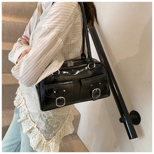 Detail of glossy black patent leather shoulder bag with silver buckles and twin pockets