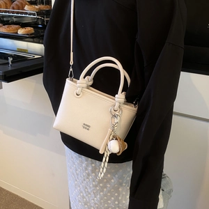 Close-up of white pebble leather handbag with creative baseball charm and metal logo