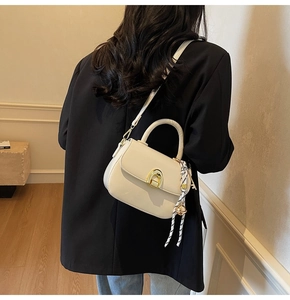 Detail of cream crossbody bag featuring a golden horseshoe clasp and decorative silk scarf
