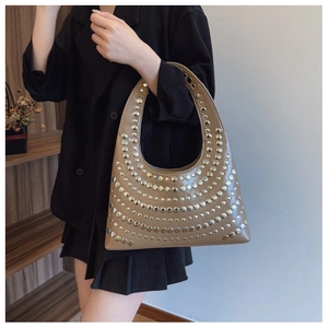 Détail d'un sac sous le bras en cuir kaki clouté porté avec une veste de costume noire