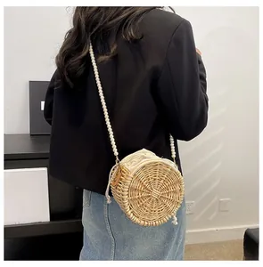 Detail of round woven straw bag with pearl strap and drawstring inner pocket on model