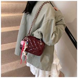 Close-up of burgundy quilted square bag with decorative floral bag charm and chain strap