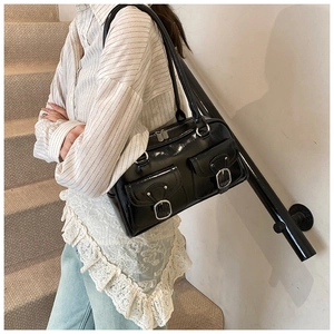 Detail of a black glossy shoulder bag with twin front pockets and silver buckle accents