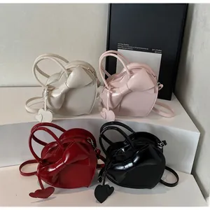Detail view of heart-shaped crossbody bags in four colors with large bow accents