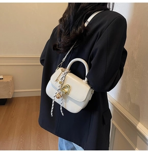 Detail of a chic cream crossbody bag with gold horseshoe lock and silk scarf on the handle