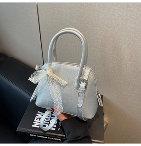 Détail du sac argenté texture litchi avec nœud en dentelle blanche et anses rondes