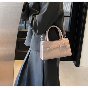 Pink leather crossbody bag worn by model featuring elegant bow and metallic buckle detail