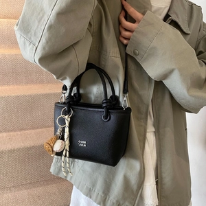 Detail of black lychee grain mini tote bag with white lettering and baseball charm