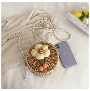 Close-up of a round straw woven bag with floral decor and decorative pearl chain strap