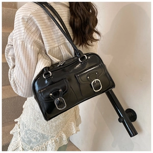 Close-up of a black patent leather shoulder bag featuring silver metal buckles and pockets
