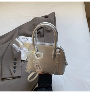 Détail du sac à main en cuir gris argenté avec texture litchi et nœud en dentelle blanche