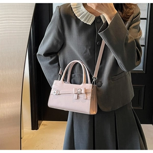 Pink crossbody bag with decorative bow and top handle shown on a grey blazer outfit