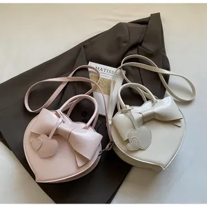 Detail of heart-shaped crossbody bags with bows in pale pink and beige PU leather